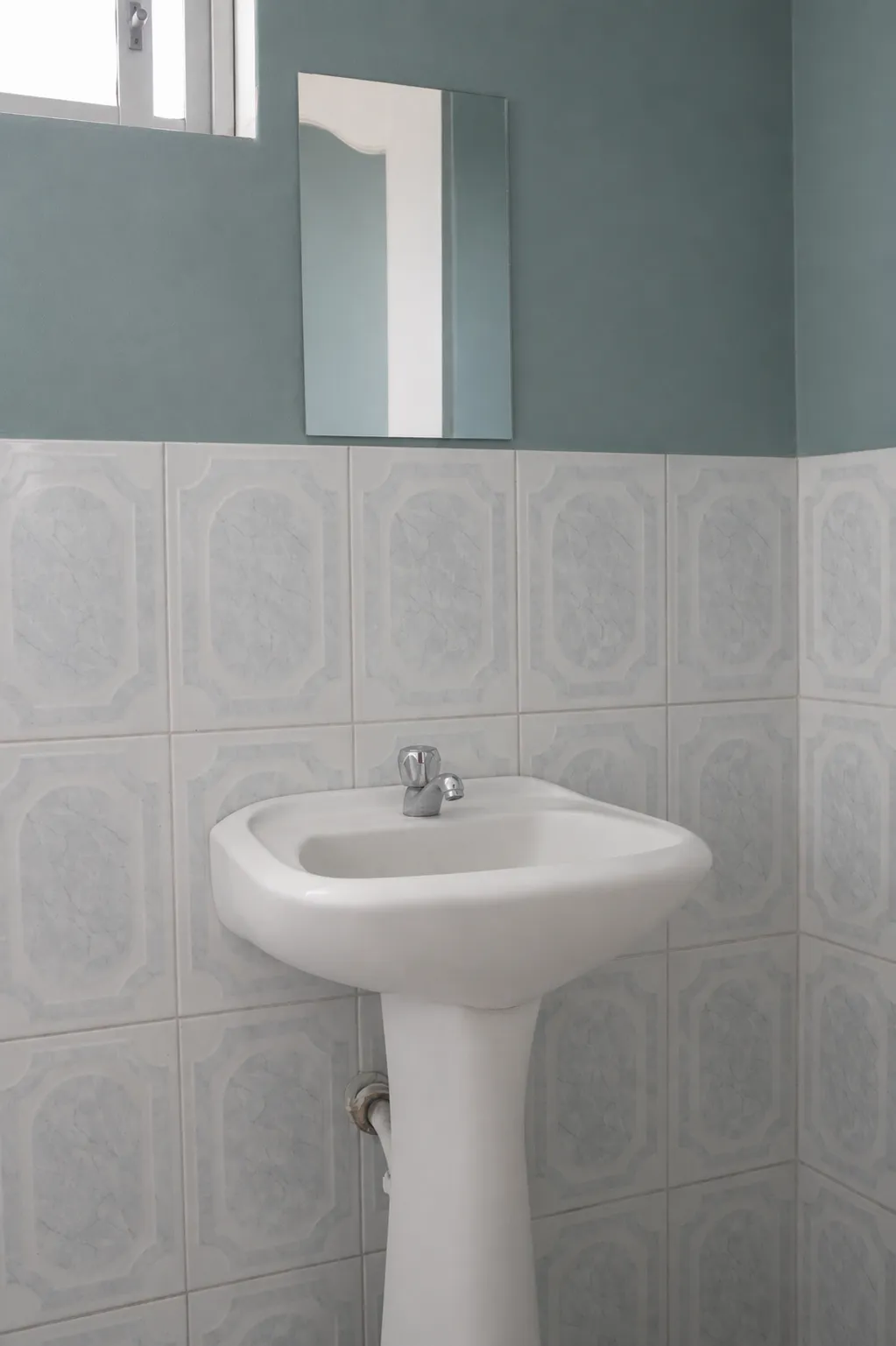 Baño con azulejo claro, espejo y lavamanos de pedestal